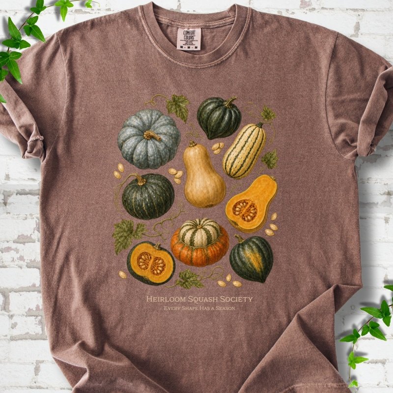 Espresso Comfort Colors® short sleeve T-shirt flat lay featuring an illustrated collection of heirloom squash, pumpkins, seeds and vines with text "Heirloom Squash Society" and "Every shape has a season"