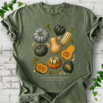Moss Comfort Colors® short sleeve T-shirt flat lay featuring an illustrated collection of heirloom squash, pumpkins, seeds and vines with text "Heirloom Squash Society" and "Every shape has a season"