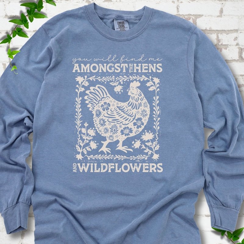 Blue Jean Comfort Colors® long sleeve T-shirt flat lay featuring a cream hen and wildflower graphic with the words You Will Find Me Amongst the Hens and Wildflowers.
