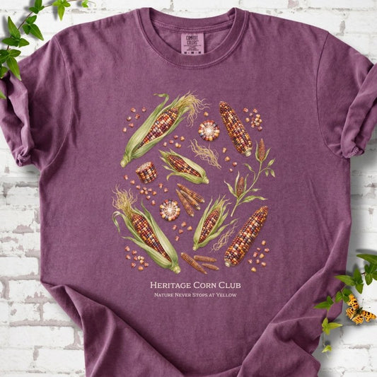 Berry Comfort Colors® short sleeve T-shirt flat lay featuring multicolored heritage corn ears, kernels and plants with text "Heritage Corn Club" and "Nature never stops at yellow"