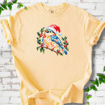 Butter T-shirt laid flat, featuring a colorful songbird in a red festive hat perched among holly leaves and berries.