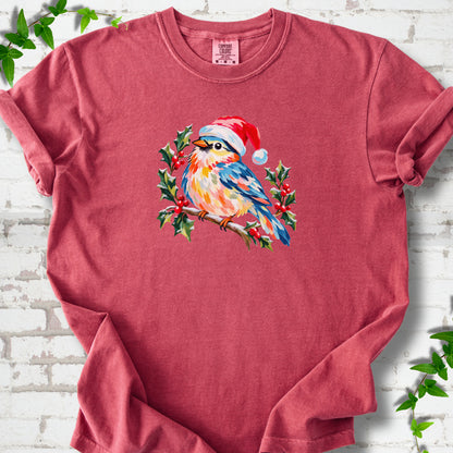 Crimson T-shirt laid flat, featuring a colorful songbird in a red festive hat perched among holly leaves and berries.