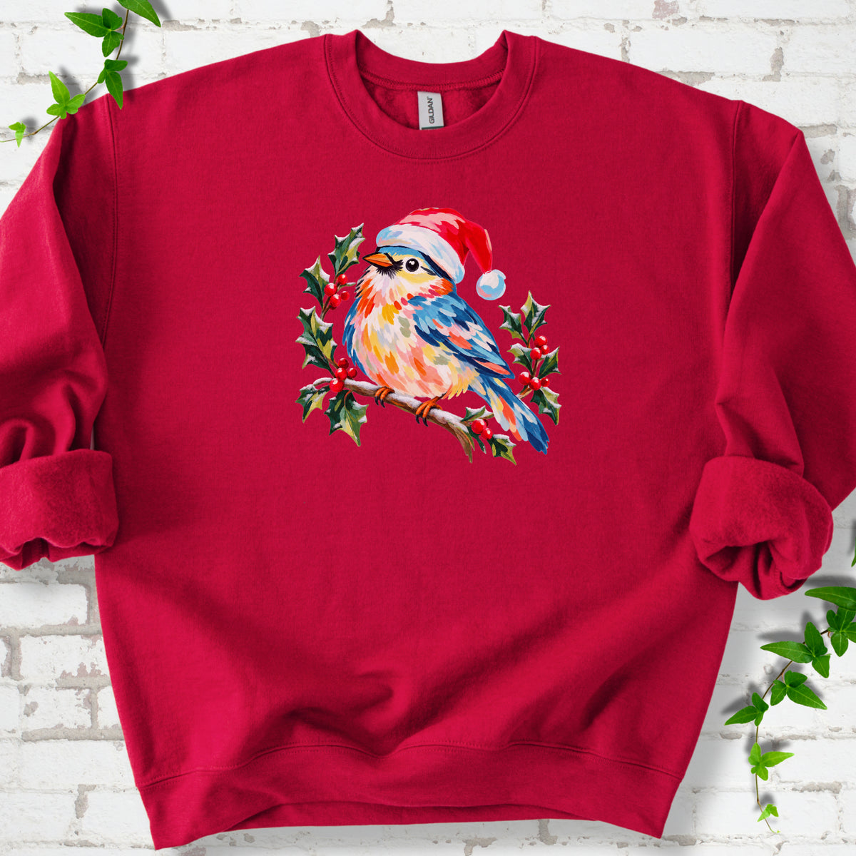 Cardinal Red classic sweatshirt laid flat, featuring a colorful songbird in a red festive hat perched among holly leaves and berries.