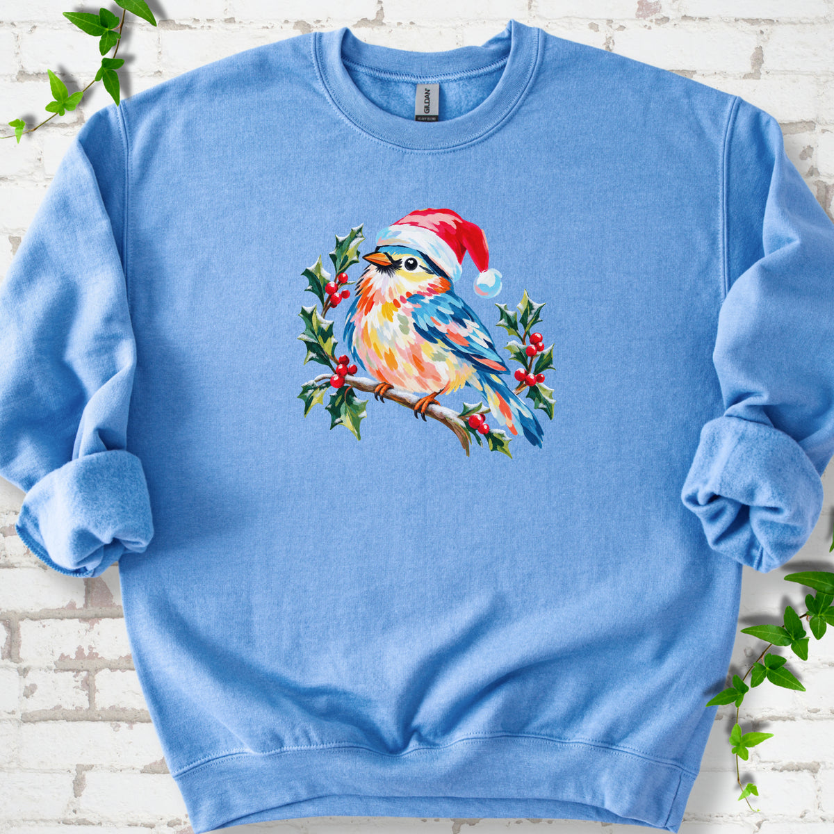 Carolina Blue classic sweatshirt laid flat, featuring a colorful songbird in a red festive hat perched among holly leaves and berries.
