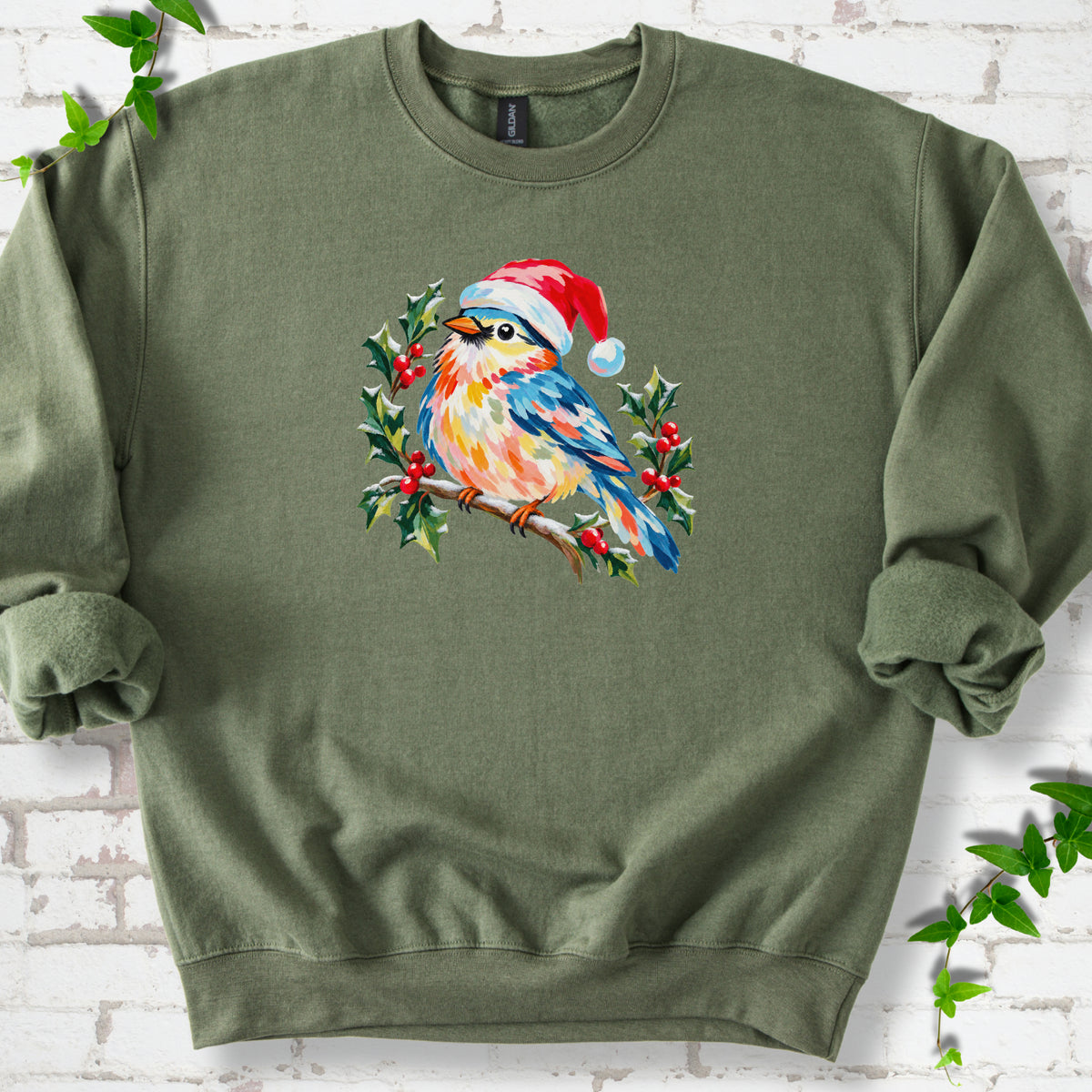 Military Green classic sweatshirt laid flat, featuring a colorful songbird in a red festive hat perched among holly leaves and berries.