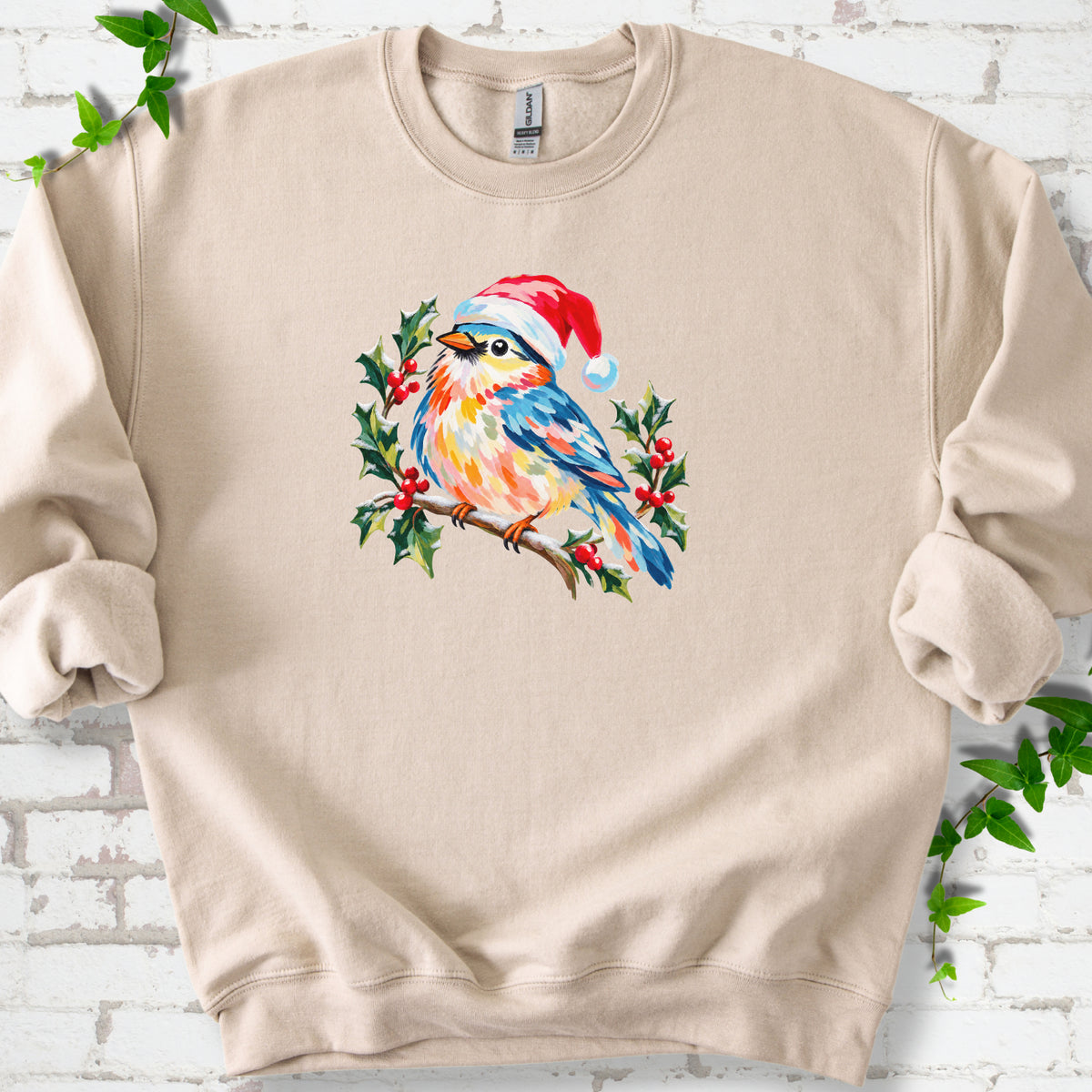 Sand classic sweatshirt laid flat, featuring a colorful songbird in a red festive hat perched among holly leaves and berries.