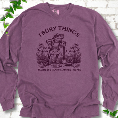 Berry Comfort Colors® long sleeve T-shirt flat lay featuring a frog with a shovel in a flower garden and the words I Bury Things.