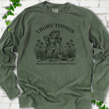 Hemp Comfort Colors® long sleeve T-shirt flat lay featuring a frog with a shovel in a flower garden and the words I Bury Things.