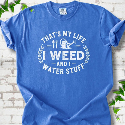 Flo Blue Comfort Colors® T-shirt flat lay featuring That's My Life I Weed and I Water Stuff text with a watering can and garden tools.