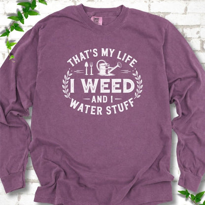 Berry Comfort Colors® long sleeve T-shirt flat lay featuring That's My Life I Weed and I Water Stuff text with a watering can and garden tools.