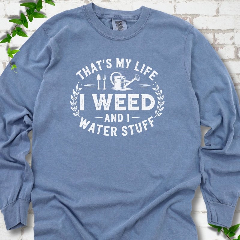 Blue Jean Comfort Colors® long sleeve T-shirt flat lay featuring That's My Life I Weed and I Water Stuff text with a watering can and garden tools.