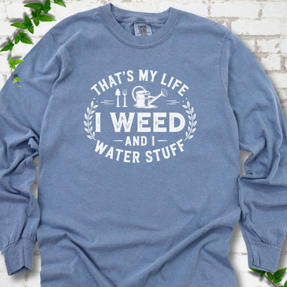 Blue Jean Comfort Colors® long sleeve T-shirt flat lay featuring That's My Life I Weed and I Water Stuff text with a watering can and garden tools.