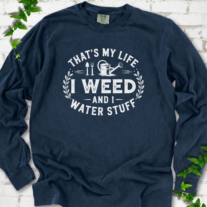 Midnight Comfort Colors® long sleeve T-shirt flat lay featuring That's My Life I Weed and I Water Stuff text with a watering can and garden tools.