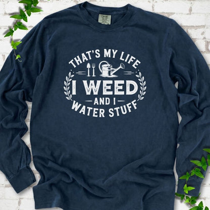Midnight Comfort Colors® long sleeve T-shirt flat lay featuring That's My Life I Weed and I Water Stuff text with a watering can and garden tools.