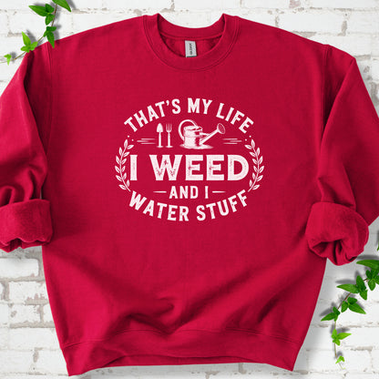 Cardinal Red Gildan® 18000 crewneck sweatshirt flat lay with garden tools and the words “That’s my life, I weed and I water stuff.”