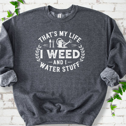 Dark Heather Gildan® 18000 crewneck sweatshirt flat lay with garden tools and the words “That’s my life, I weed and I water stuff.”