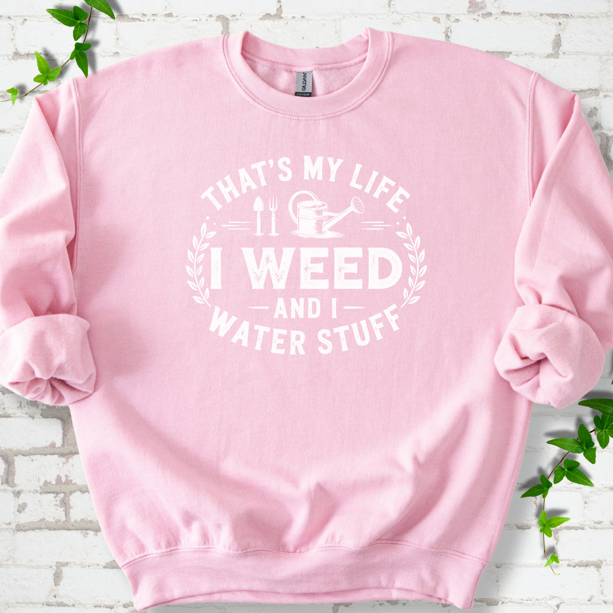 Light Pink Gildan® 18000 crewneck sweatshirt flat lay with garden tools and the words “That’s my life, I weed and I water stuff.”