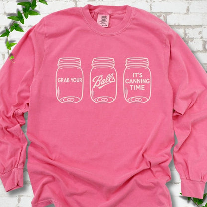 Crunchberry long sleeve T-shirt flat lay with cream line-art illustrations of three mason jars in a row, the first reading "Grab your", the middle with "Balls" in script and the last reading "It's canning time", on white brick with ivy sprigs.