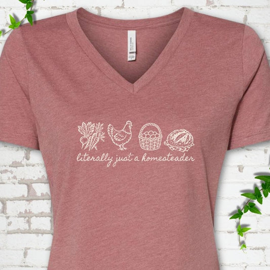 Heather Mauve women's V-neck T-shirt flat lay with cream line-art icons in a row of carrots and radishes, a hen, a basket of eggs and a loaf of bread above the script words "literally just a homesteader", on white brick with ivy sprigs.