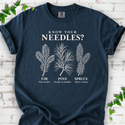 Midnight T-shirt laid flat, showing cream fir, pine and spruce needle illustrations beneath "Know Your Needles?" with identification labels.
