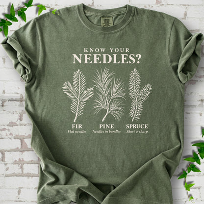 Moss T-shirt laid flat, showing cream fir, pine and spruce needle illustrations beneath "Know Your Needles?" with identification labels.
