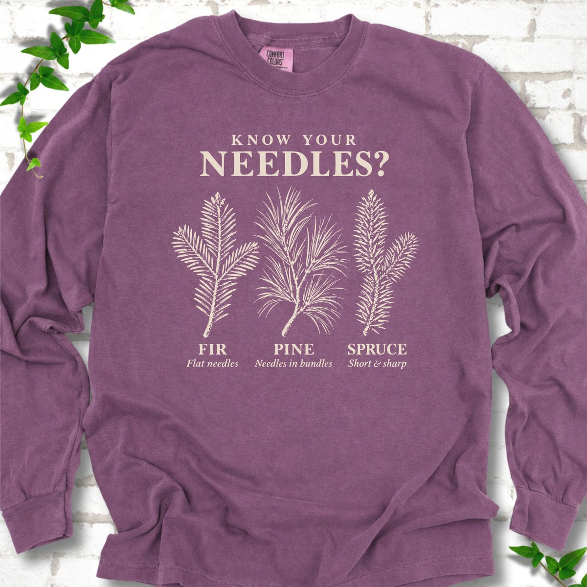 Berry long sleeve tee laid flat, showing cream fir, pine and spruce needle illustrations beneath "Know Your Needles?" with identification labels.