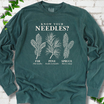 Blue Spruce long sleeve tee laid flat, showing cream fir, pine and spruce needle illustrations beneath "Know Your Needles?" with identification labels.