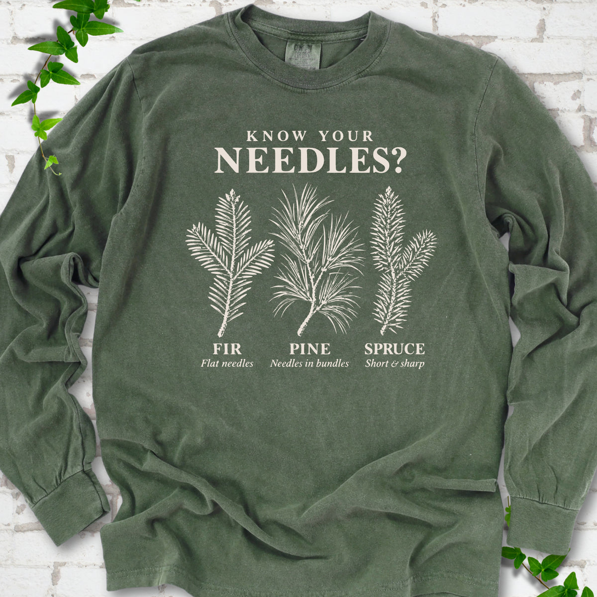 Hemp long sleeve tee laid flat, showing cream fir, pine and spruce needle illustrations beneath "Know Your Needles?" with identification labels.