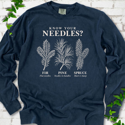 Midnight long sleeve tee laid flat, showing cream fir, pine and spruce needle illustrations beneath "Know Your Needles?" with identification labels.
