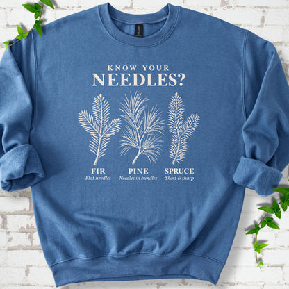 Indigo Blue classic sweatshirt laid flat, showing cream fir, pine and spruce needle illustrations beneath "Know Your Needles?" with identification labels.