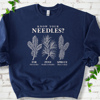 Navy classic sweatshirt laid flat, showing cream fir, pine and spruce needle illustrations beneath "Know Your Needles?" with identification labels.