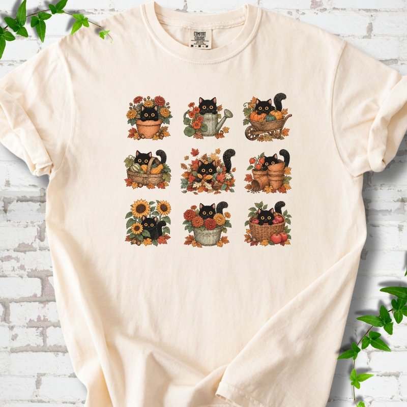 Front flat lay of a Ivory short sleeve T-shirt with a nine-panel grid of black cats among fall garden flowers, pots and leaves, on white brick with green leafy sprigs.