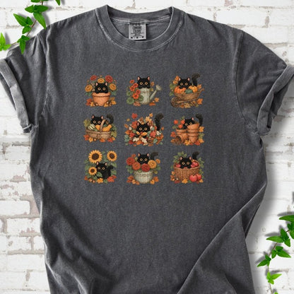 Front flat lay of a Pepper short sleeve T-shirt with a nine-panel grid of black cats among fall garden flowers, pots and leaves, on white brick with green leafy sprigs.
