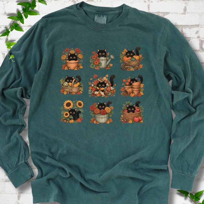 Front flat lay of a Blue Spruce long sleeve T-shirt with a nine-panel grid of black cats among fall garden flowers, pots and leaves, on white brick with green leafy sprigs.