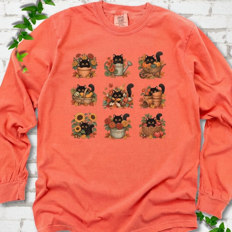 Front flat lay of a Bright Salmon long sleeve T-shirt with a nine-panel grid of black cats among fall garden flowers, pots and leaves, on white brick with green leafy sprigs.