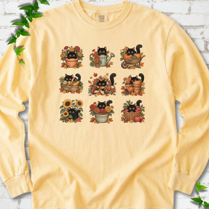 Front flat lay of a Butter long sleeve T-shirt with a nine-panel grid of black cats among fall garden flowers, pots and leaves, on white brick with green leafy sprigs.