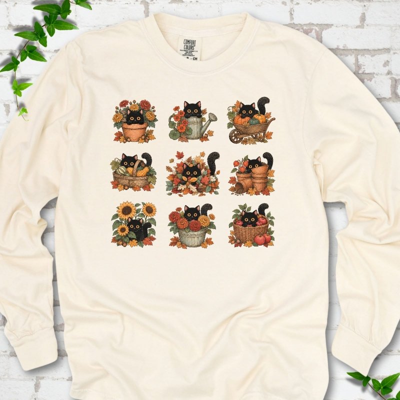 Front flat lay of a Ivory long sleeve T-shirt with a nine-panel grid of black cats among fall garden flowers, pots and leaves, on white brick with green leafy sprigs.