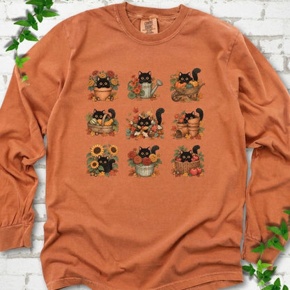 Front flat lay of a Yam long sleeve T-shirt with a nine-panel grid of black cats among fall garden flowers, pots and leaves, on white brick with green leafy sprigs.