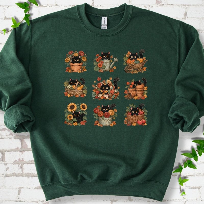 Front flat lay of a Forest Green crewneck sweatshirt with a nine-panel grid of black cats among fall garden flowers, pots and leaves, on white brick with green leafy sprigs.