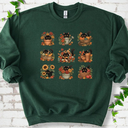 Front flat lay of a Forest Green crewneck sweatshirt with a nine-panel grid of black cats among fall garden flowers, pots and leaves, on white brick with green leafy sprigs.