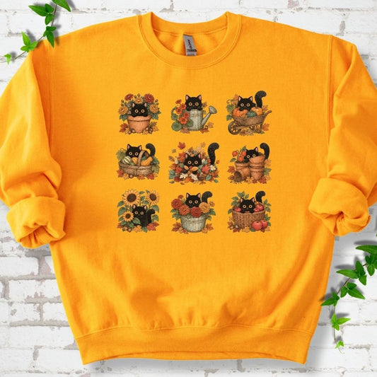 Front flat lay of a Gold crewneck sweatshirt with a nine-panel grid of black cats among fall garden flowers, pots and leaves, on white brick with green leafy sprigs.