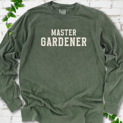 Hemp long sleeve T-shirt laid flat on white brick with greenery, showing the cream words 'Master Gardener' centered on the chest.