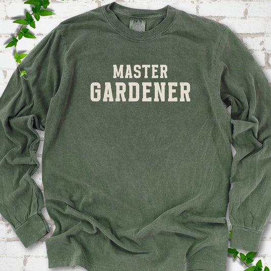 Hemp long sleeve T-shirt laid flat on white brick with greenery, showing the cream words 'Master Gardener' centered on the chest.