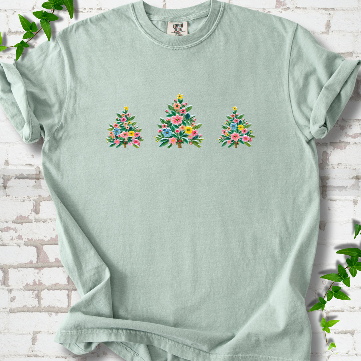 Bay short-sleeve T-shirt laid flat on white brick with three flower-filled trees centered on the front.