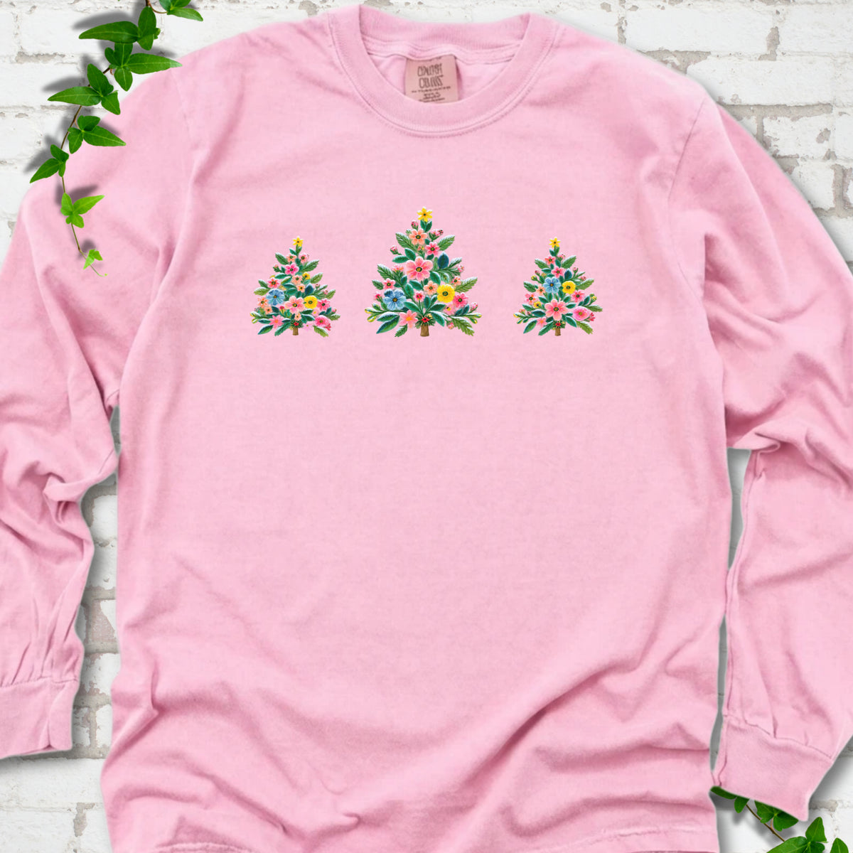 Blossom long-sleeve T-shirt laid flat on white brick with three flower-filled trees centered on the front.