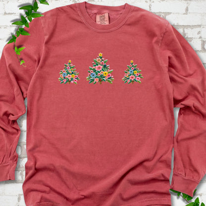Crimson long-sleeve T-shirt laid flat on white brick with three flower-filled trees centered on the front.
