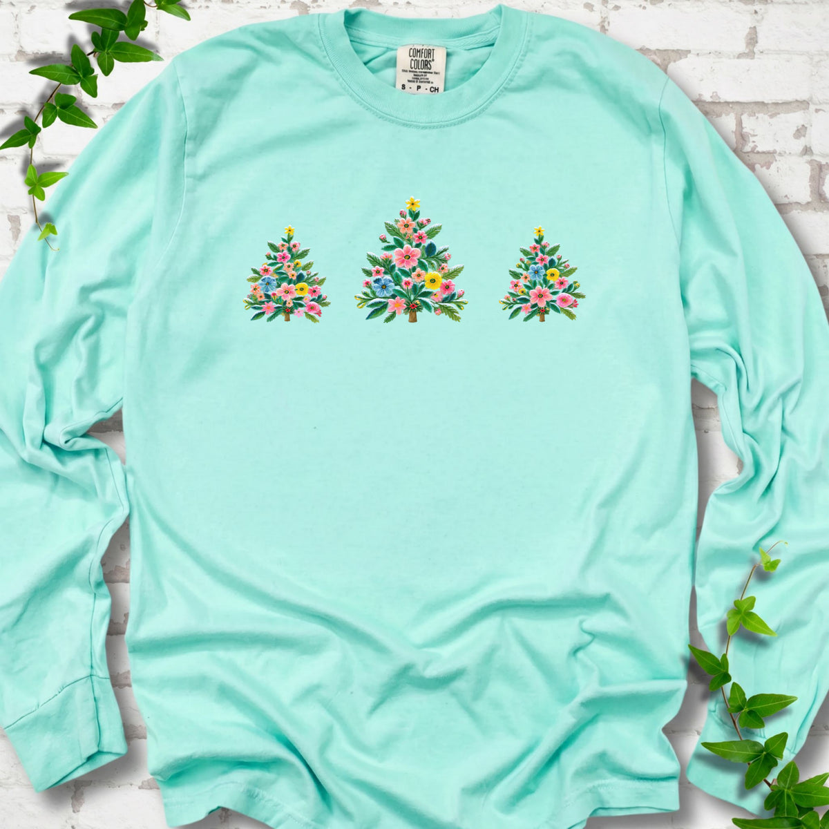 Island Reef long-sleeve T-shirt laid flat on white brick with three flower-filled trees centered on the front.