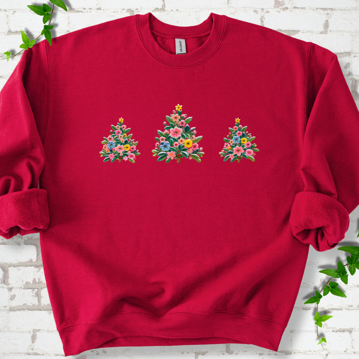 Cardinal red crewneck sweatshirt laid flat on white brick with three flower-filled trees centered on the front.