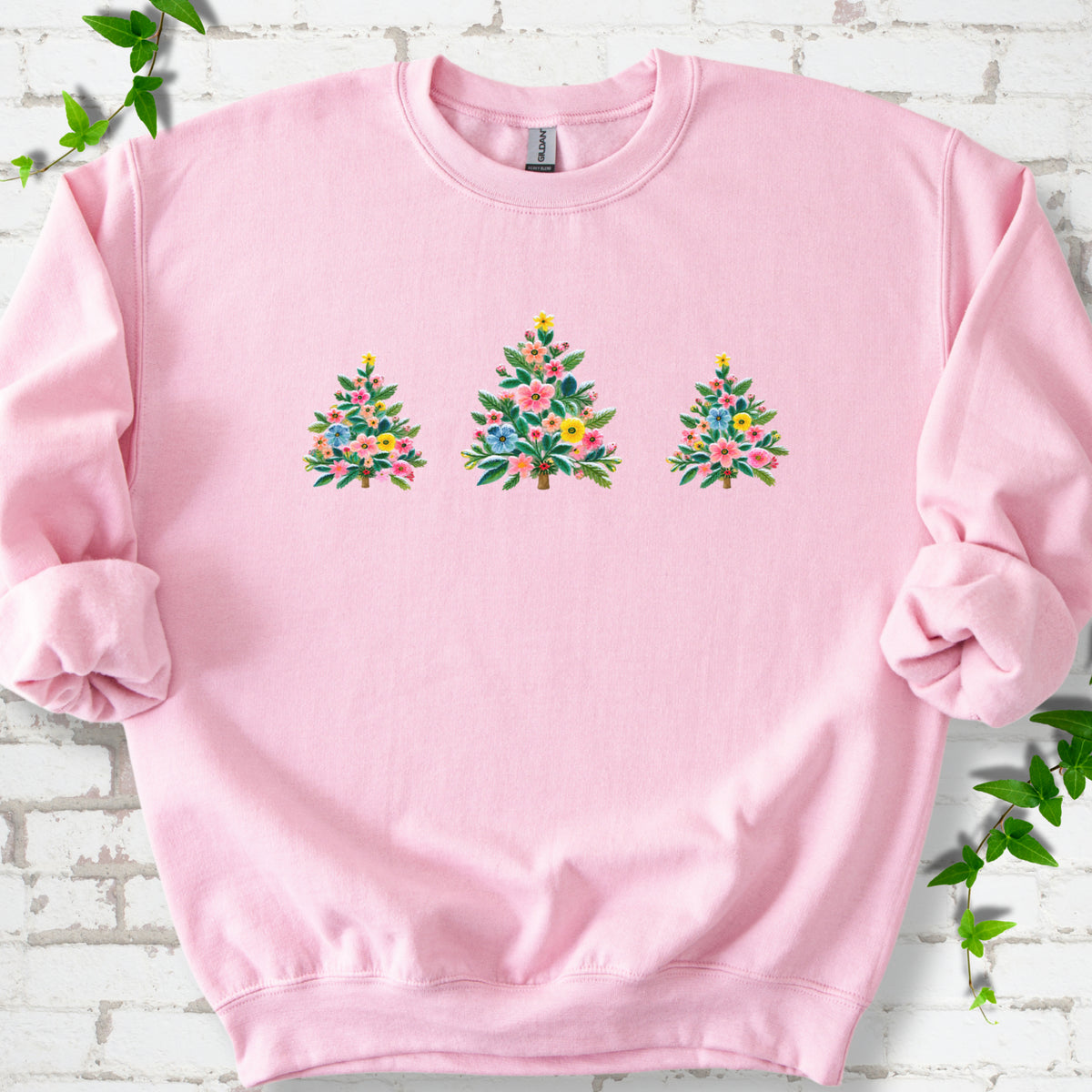 Light Pink crewneck sweatshirt laid flat on white brick with three flower-filled trees centered on the front.