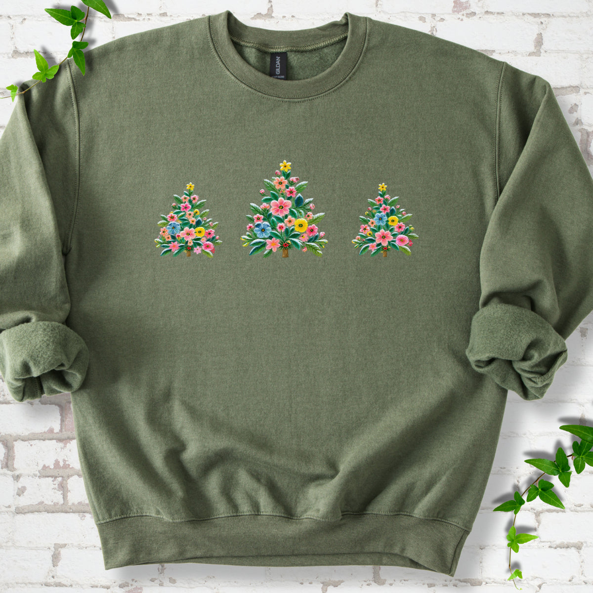 Military green crewneck sweatshirt laid flat on white brick with three flower-filled trees centered on the front.